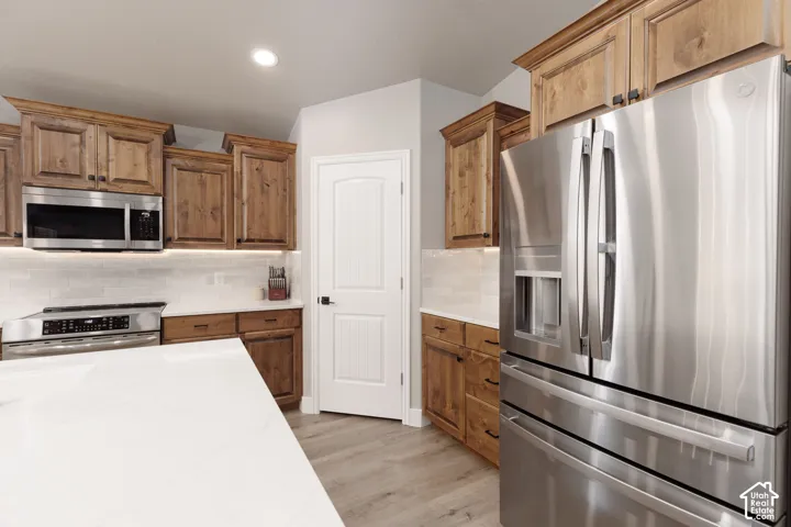 Kitchen featuring wood cabinetry, stainless steel appliances, white subway tile backsplash, white countertops, and LVP flooring