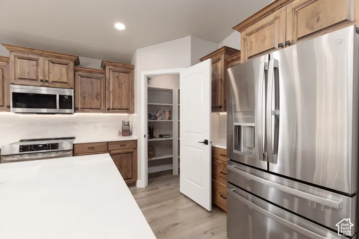Kitchen featuring wood cabinetry, stainless steel appliances, white subway tile backsplash, white countertops, and LVP flooring
