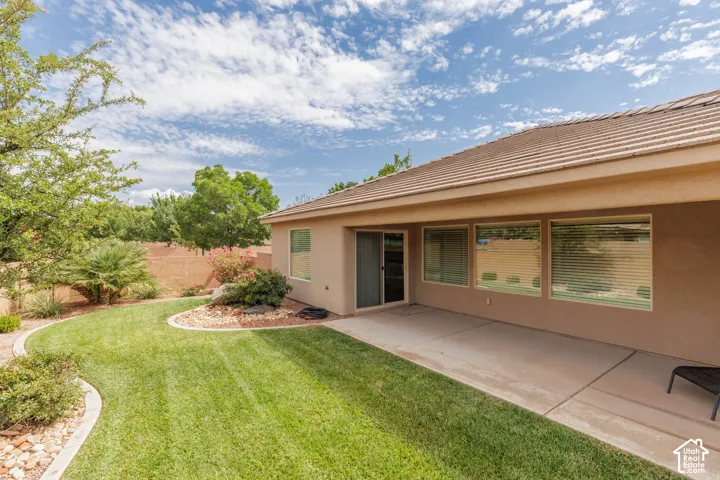 Expansive backyard featuring a manicured lawn, established landscaping, large covered patio and a privacy wall