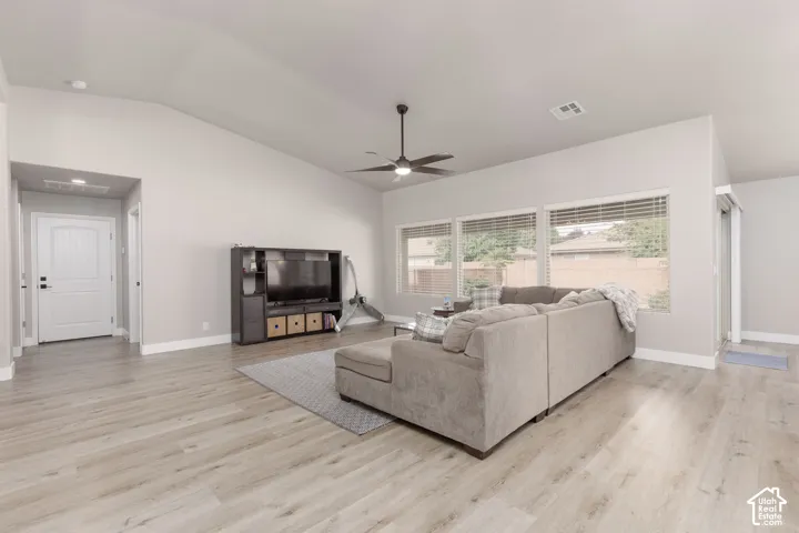 Spacious living area featuring vaulted ceilings, a ceiling fan with integrated lighting, and multiple windows with horizontal blinds
