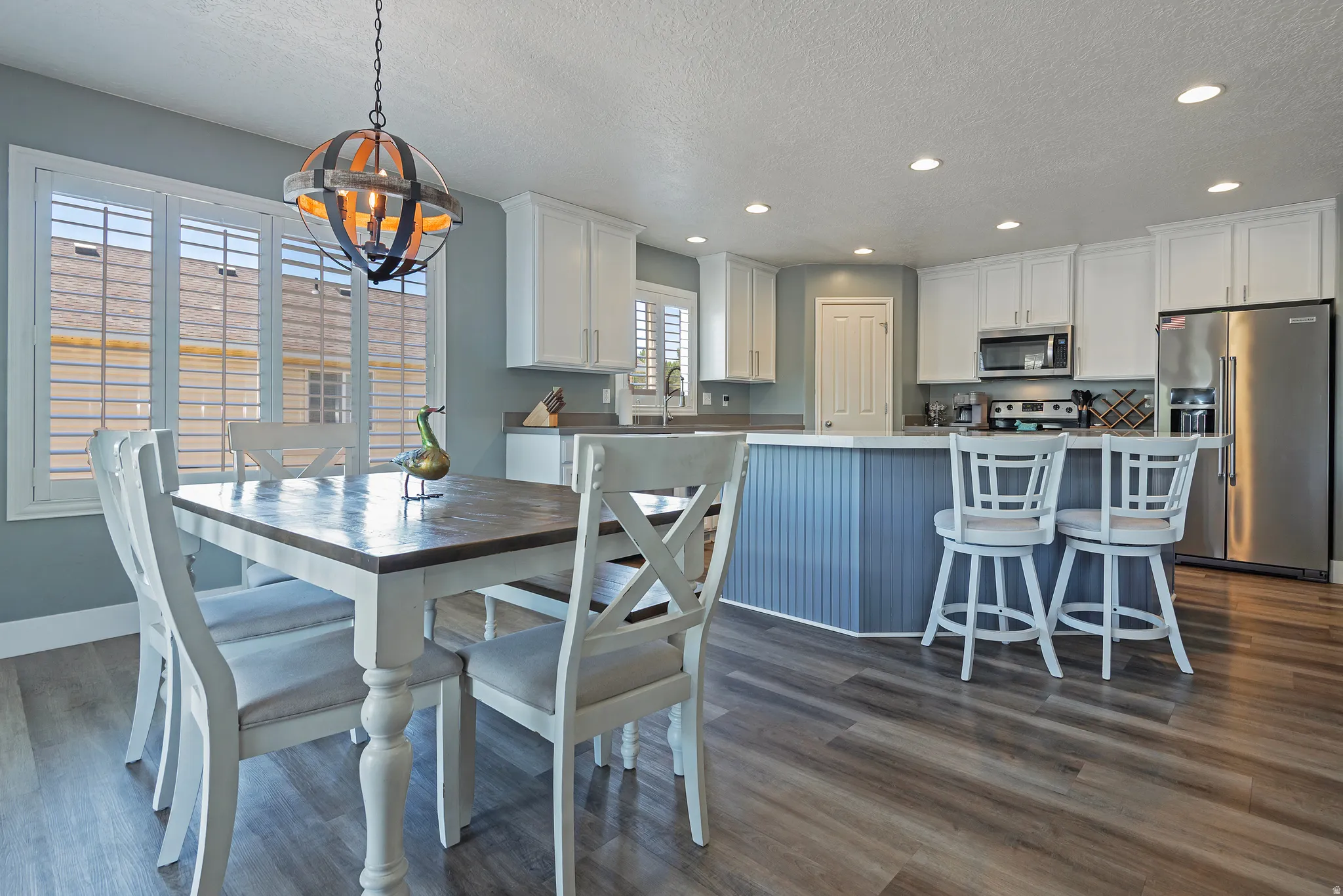 Open-concept kitchen and dining area featuring wood-finish flooring, white cabinetry, recessed lighting, stainless steel appliances, and a central island with beadboard paneling