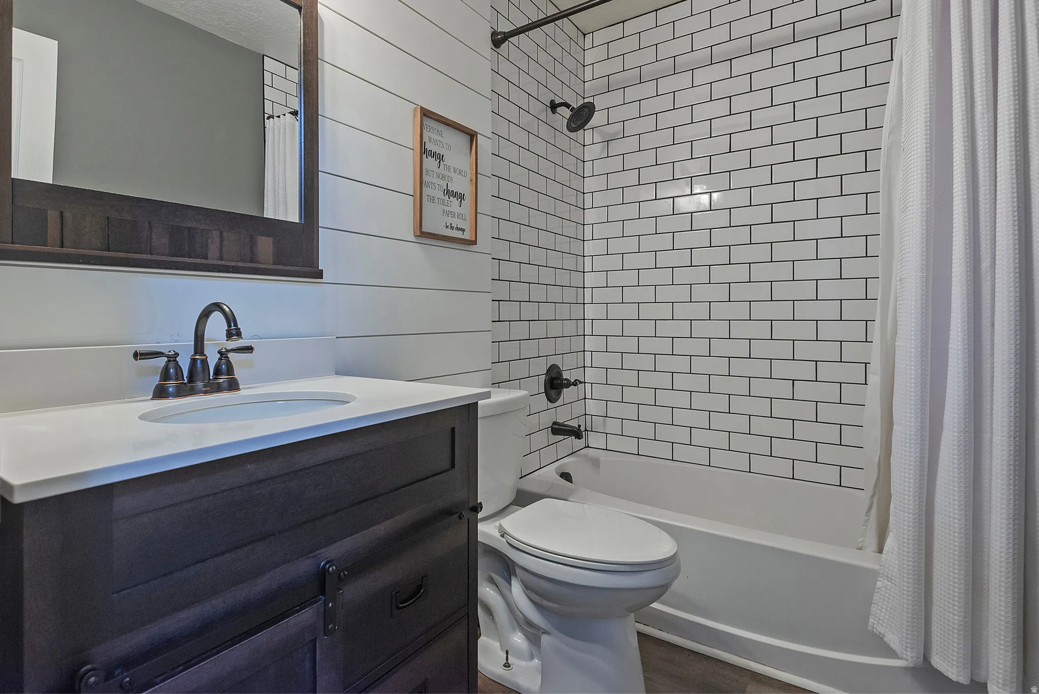 Bathroom featuring a dark wood-finish vanity with a white countertop and oval sink, dark bronze fixtures, white shiplap wall paneling, and subway tile shower surround