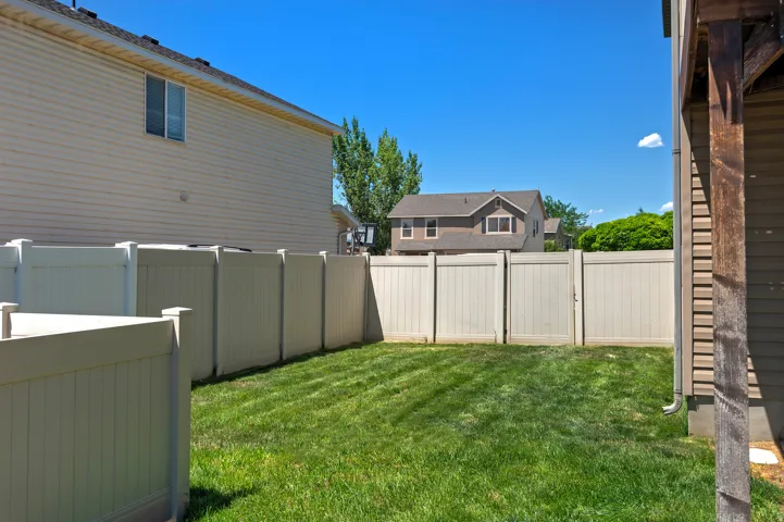 Fenced backyard with a manicured lawn, featuring a light-colored privacy fence and an external wood-finish column