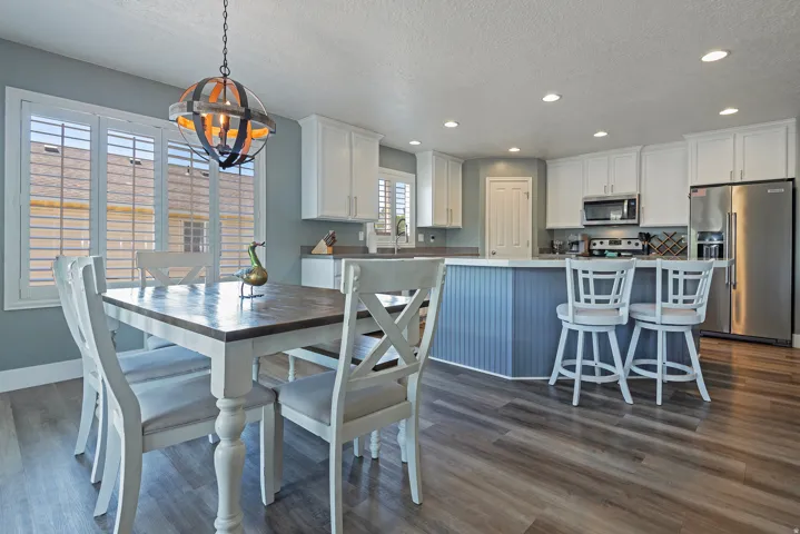 Open-concept kitchen and dining area featuring wood-finish flooring, white cabinetry, recessed lighting, stainless steel appliances, and a central island with beadboard paneling
