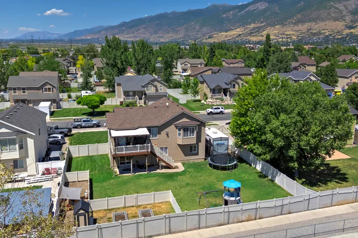 Expansive backyard featuring a green lawn, white vinyl fencing, and a covered second-story deck with stairs to the ground level