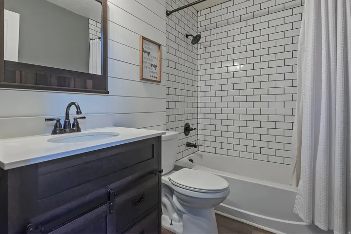 Bathroom featuring a dark wood-finish vanity with a white countertop and oval sink, dark bronze fixtures, white shiplap wall paneling, and subway tile shower surround