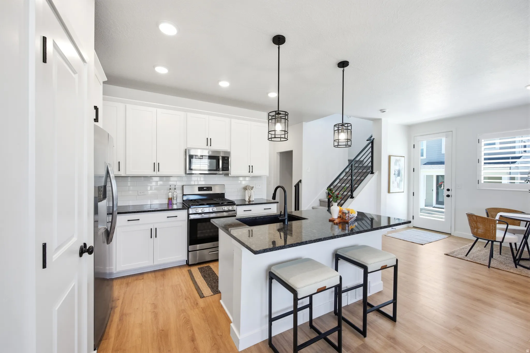 Kitchen featuring white shaker cabinetry, stainless steel appliances, dark granite countertops, a subway tile backsplash, and wood-finish flooring