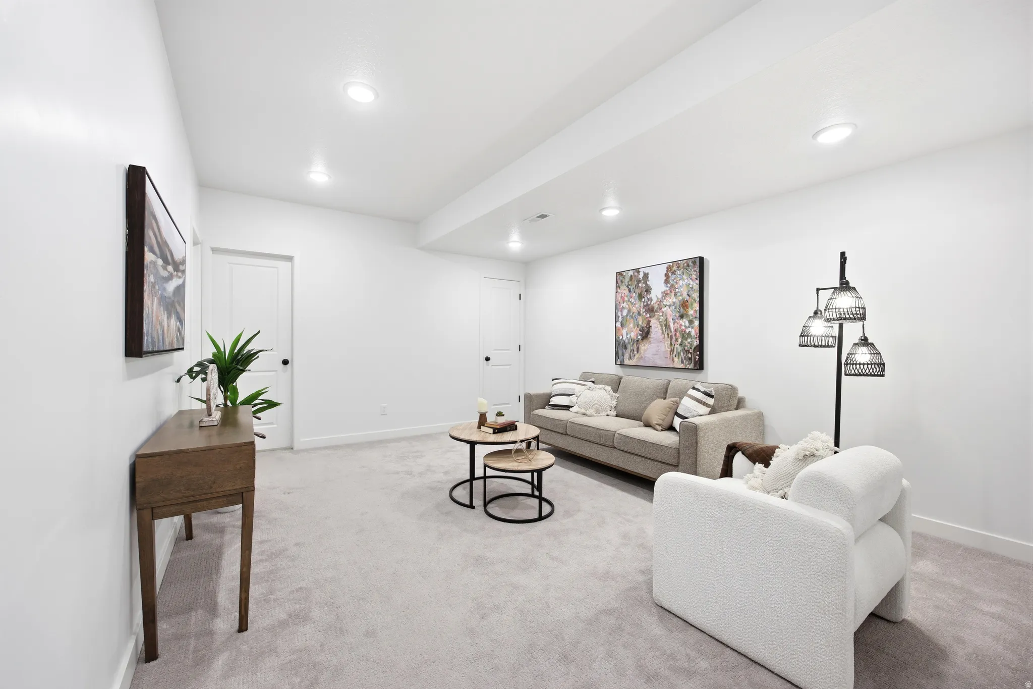 Spacious interior room featuring light gray carpeting, recessed ceiling lighting, crisp white walls, and white interior doors with black hardware