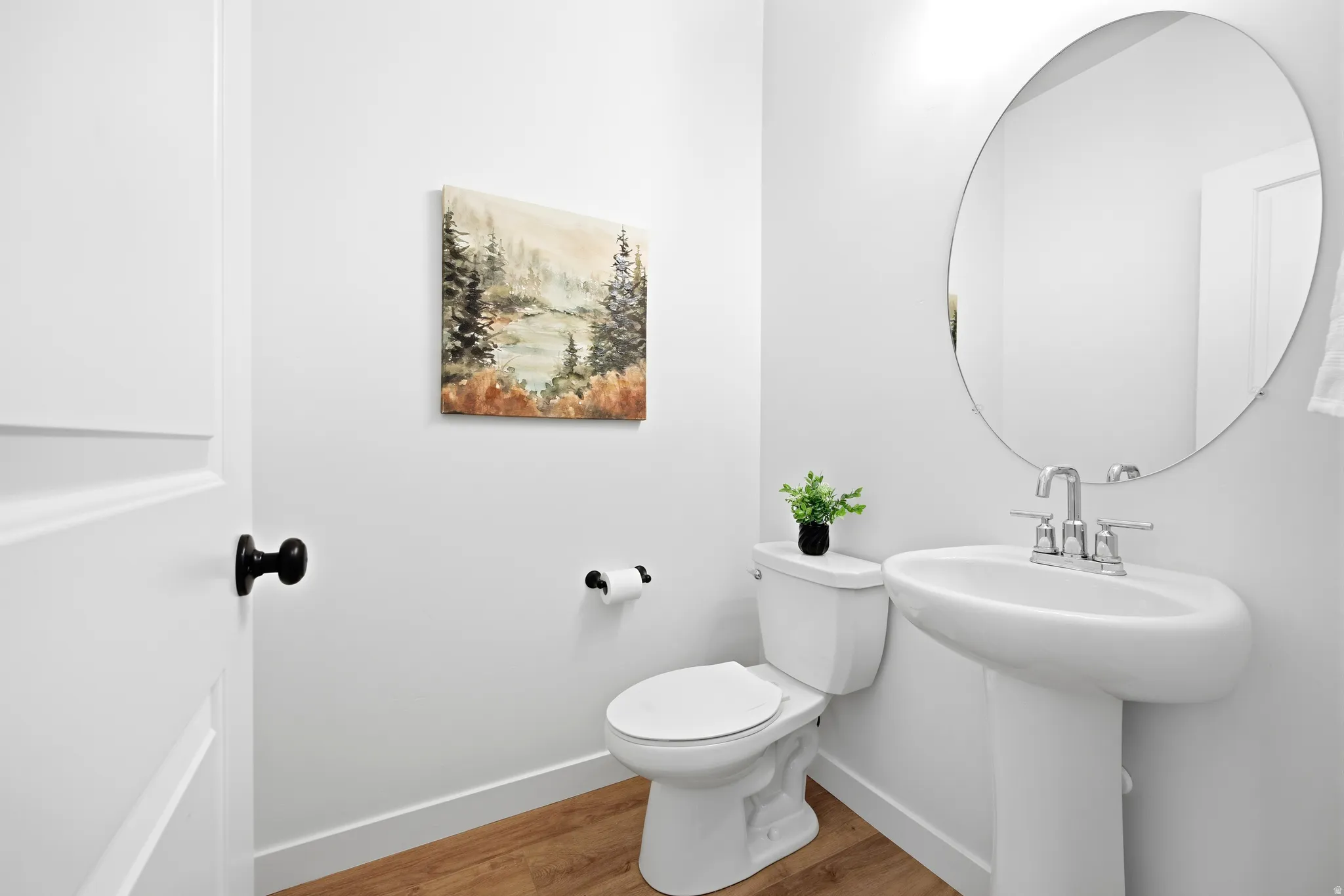Pedestal sink with chrome faucet, circular mirror, and white toilet