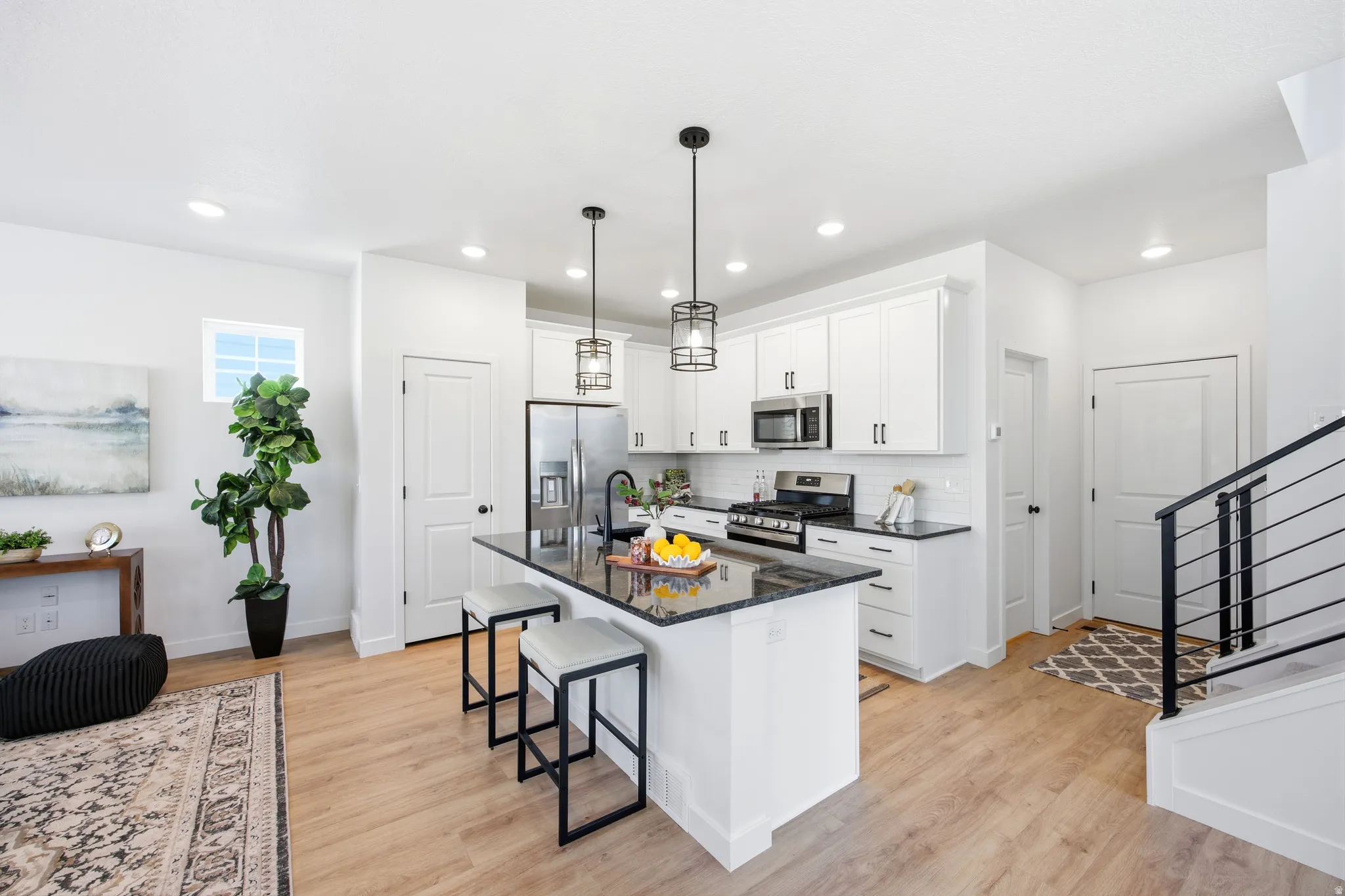 Open-concept kitchen featuring white cabinetry, stainless steel appliances, a center island with dark countertop, and pendant lighting