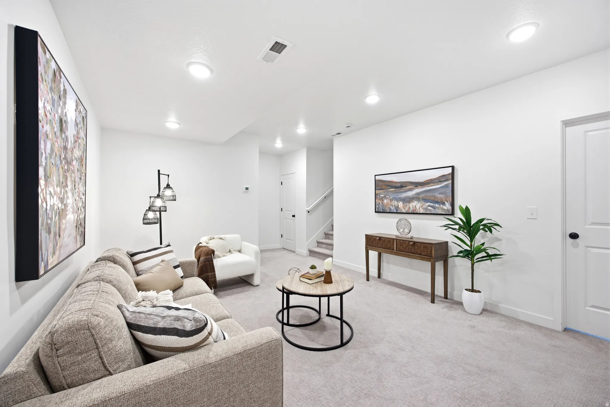 Spacious living area featuring light gray carpeting, recessed ceiling lighting, a contemporary console table, and a white paneled door