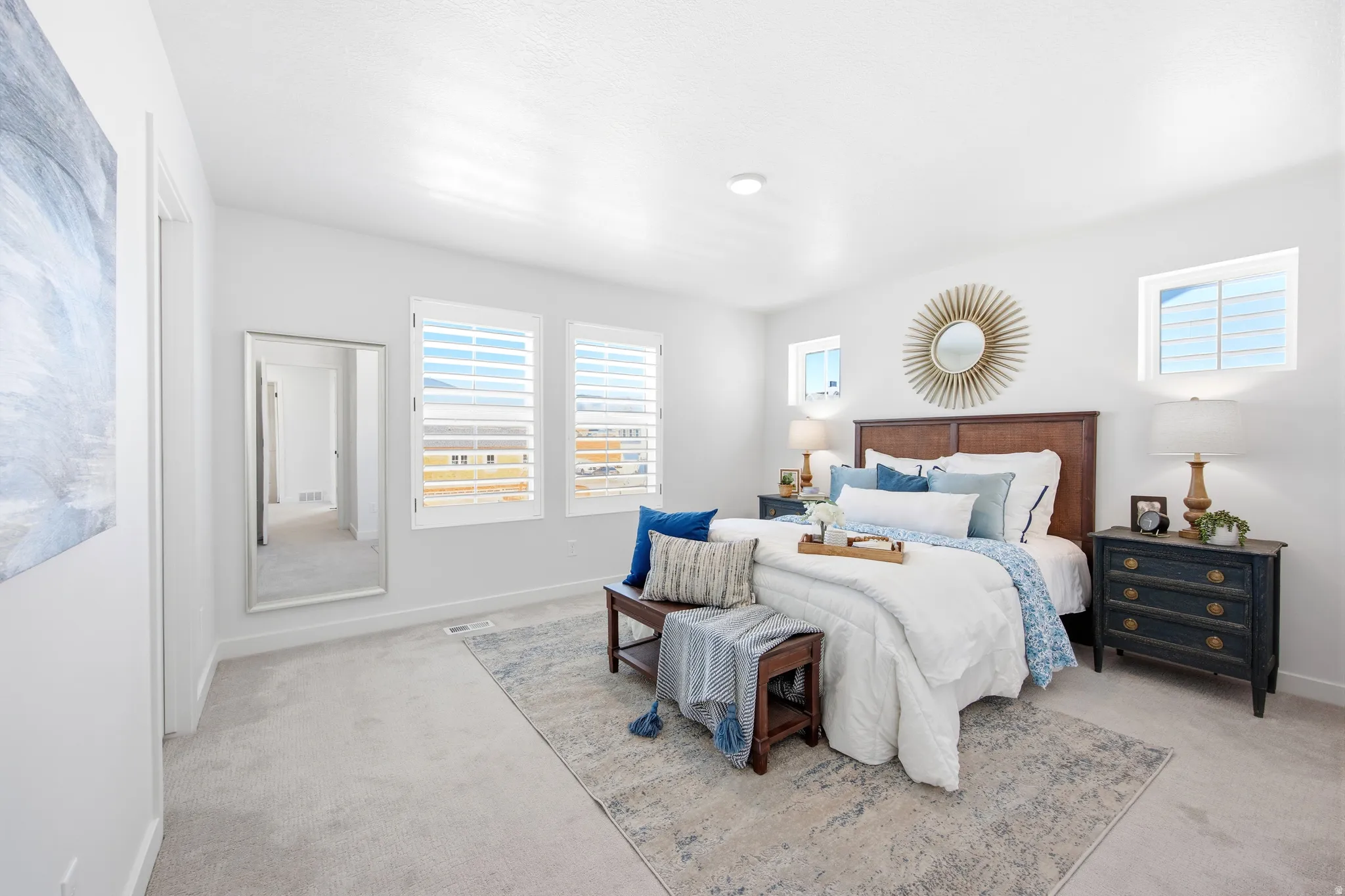White walls and light-toned carpeting enhance the brightness of this bedroom, featuring multiple windows with white plantation shutters