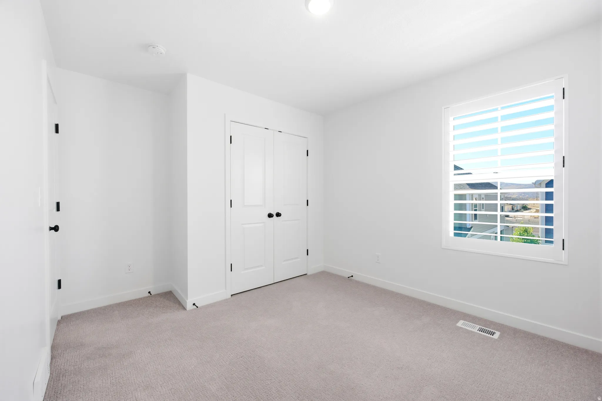 Bright interior space featuring a window with integrated blinds, plush carpeting, and white walls