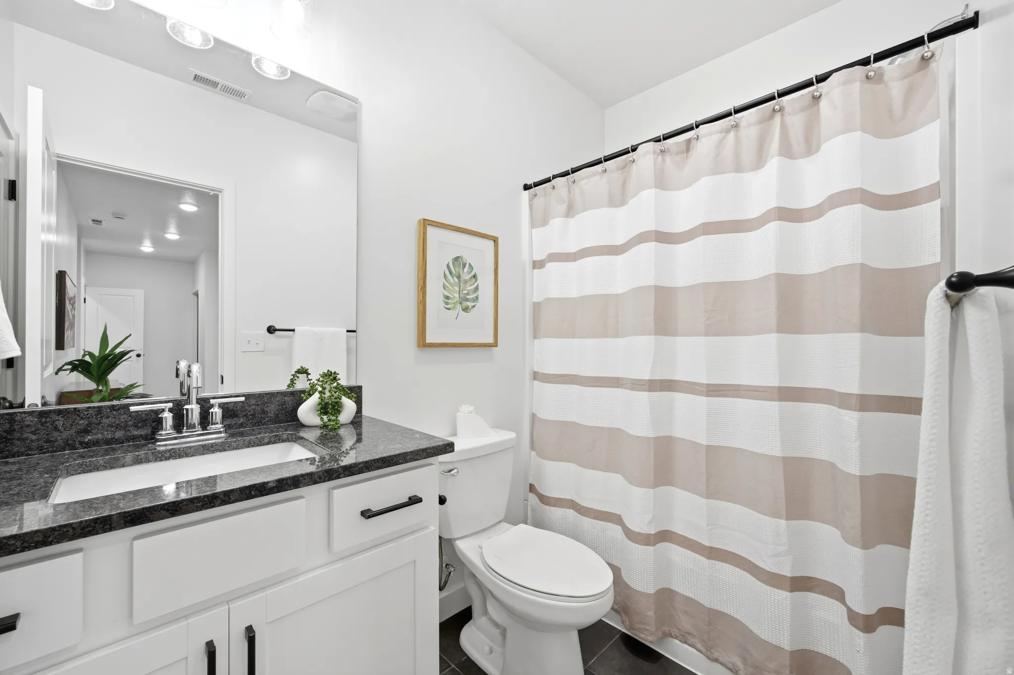 Bathroom featuring a dark speckled countertop, white vanity with black hardware, and an integrated rectangular sink