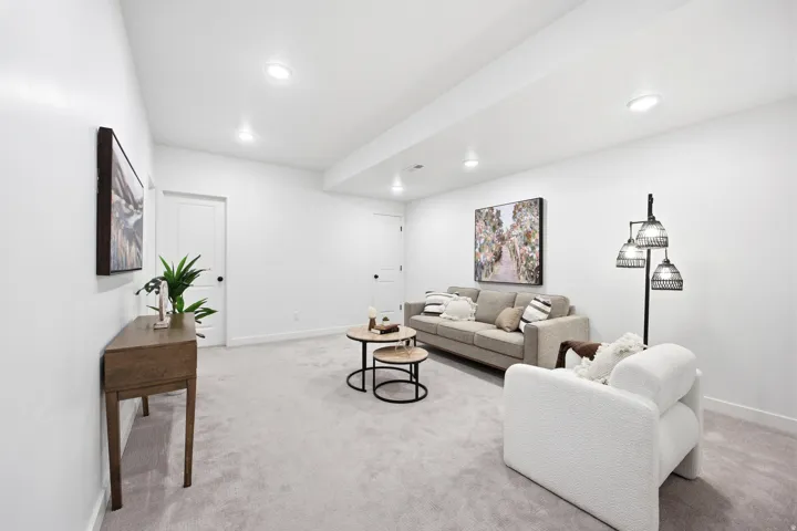 Spacious interior room featuring light gray carpeting, recessed ceiling lighting, crisp white walls, and white interior doors with black hardware