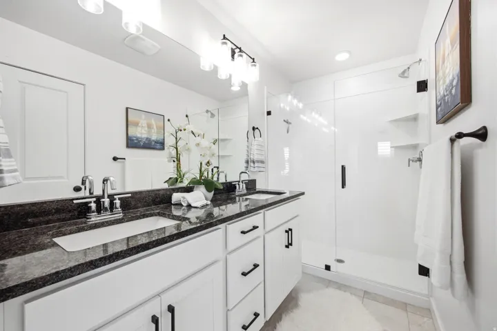 Modern bathroom featuring a dual vanity with a dark granite countertop, white cabinetry with black hardware, and an expansive mirror