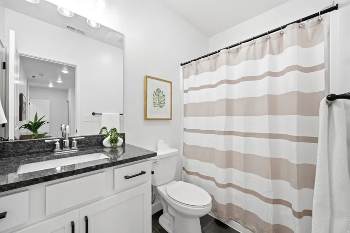 Bathroom featuring a dark speckled countertop, white vanity with black hardware, and an integrated rectangular sink