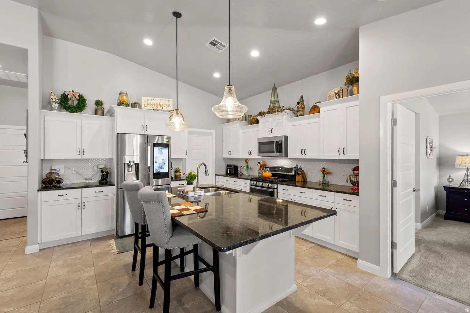 Open-concept kitchen featuring white cabinetry, dark stone countertops, a tile backsplash, stainless steel appliances, and a large island with seating