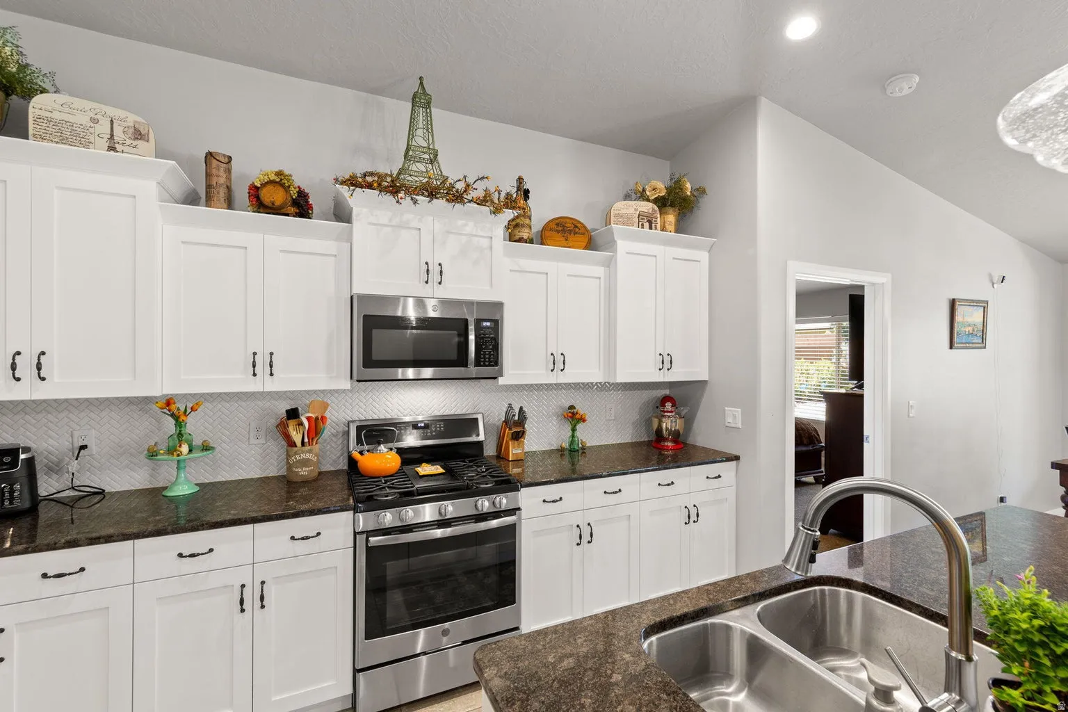 Kitchen featuring white shaker-style cabinetry, stainless steel appliances, dark stone countertops, a herringbone tile backsplash, and a double basin sink with a gooseneck faucet
