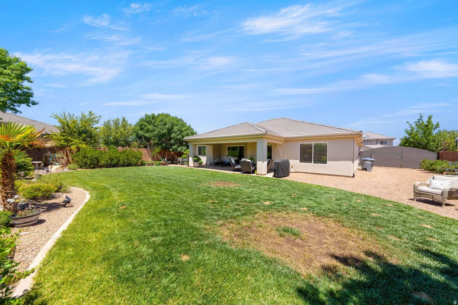 Expansive backyard featuring a manicured lawn, established landscaping, and a covered patio area