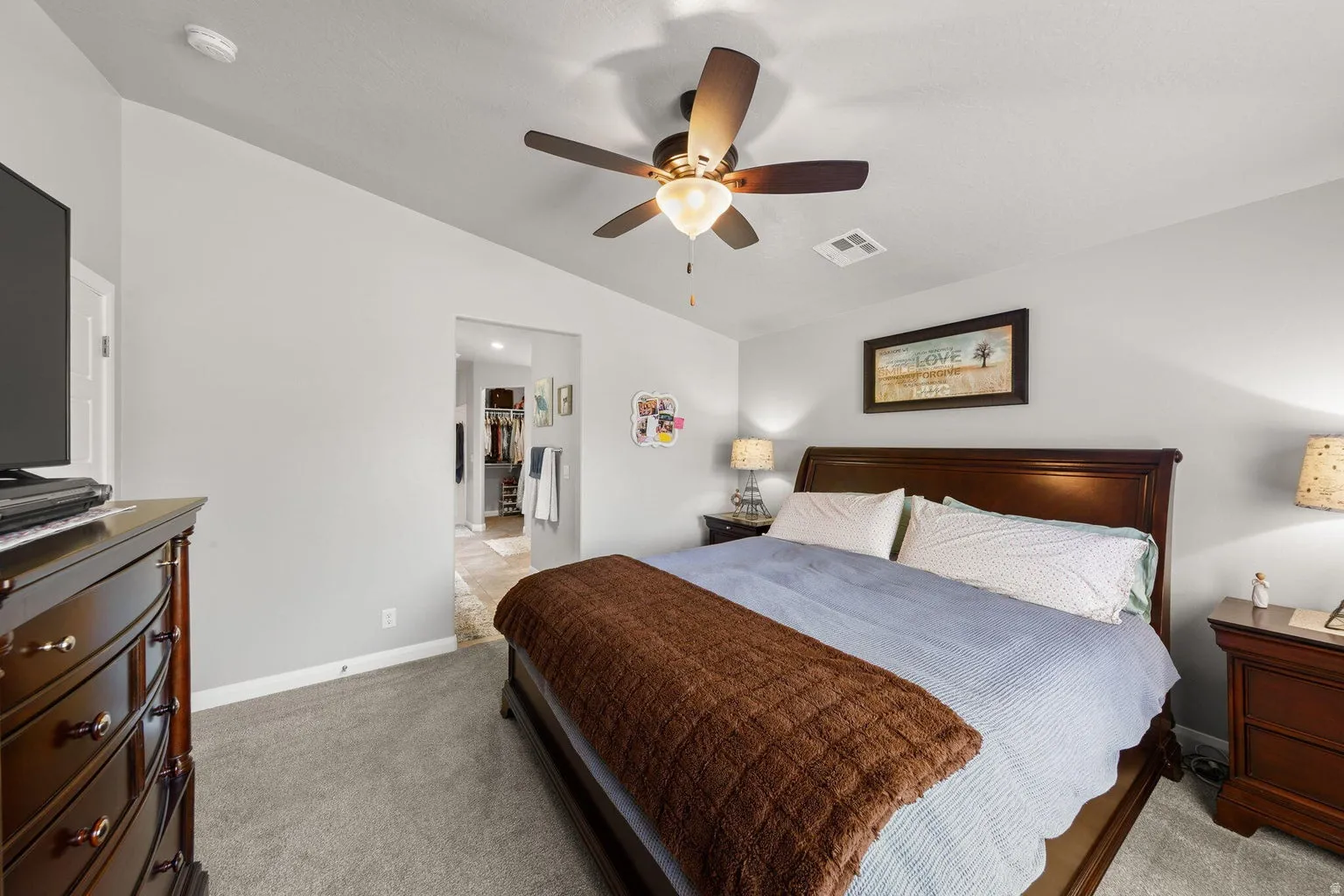 Carpeted bedroom featuring a ceiling fan with integrated lighting, light gray wall paint, and a doorway leading to an adjacent tiled space
