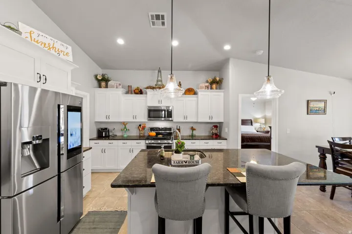 Kitchen featuring a large central island with seating, white cabinetry, dark countertops, and stainless steel appliances