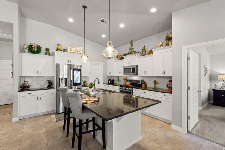 Open-concept kitchen featuring white cabinetry, dark stone countertops, a tile backsplash, stainless steel appliances, and a large island with seating