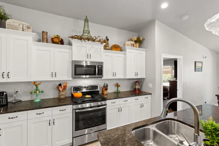 Kitchen featuring white shaker-style cabinetry, stainless steel appliances, dark stone countertops, a herringbone tile backsplash, and a double basin sink with a gooseneck faucet