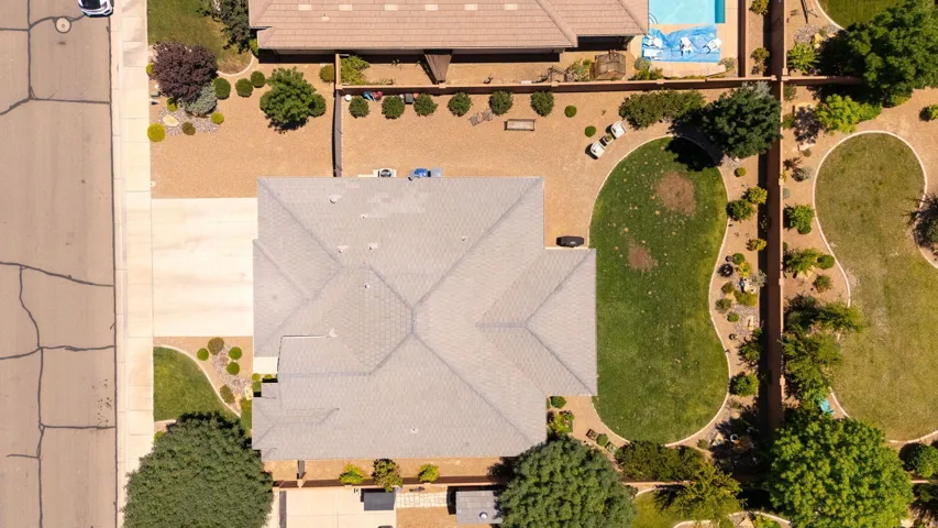 Aerial perspective showcasing the property's expansive lot with a multi-level roofline, extensive gravel landscaping, mature trees, and a sculpted lawn area