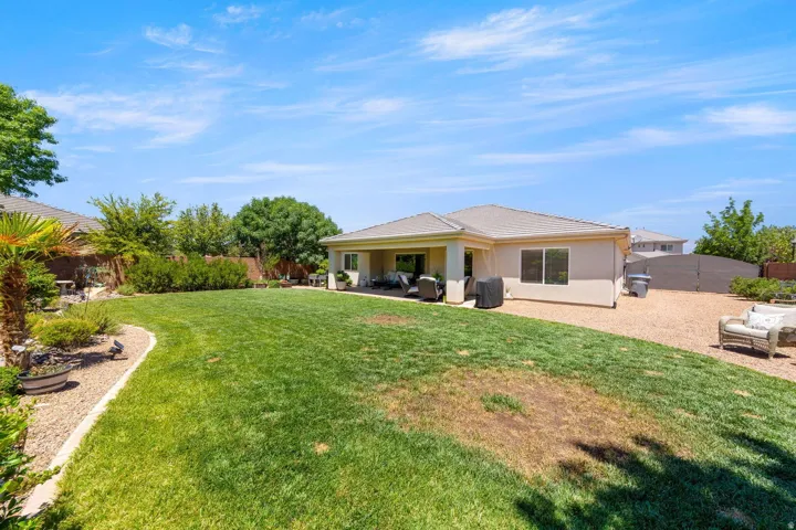 Expansive backyard featuring a manicured lawn, established landscaping, and a covered patio area