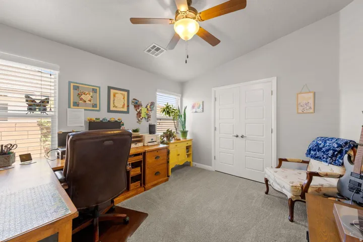 Carpeted room featuring dual windows with blinds, a ceiling fan with integrated lighting, and double panel doors