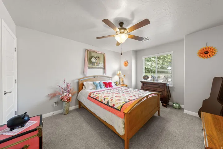 Bright room featuring light gray walls, plush gray carpeting, a multi-pane window with horizontal blinds, a ceiling fan with integrated lighting, and a paneled interior door