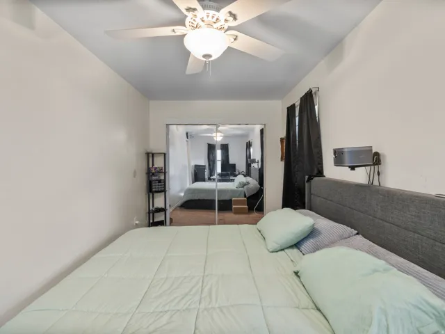 Bedroom featuring a ceiling fan with integrated lighting, mirrored sliding closet doors, and light-colored walls