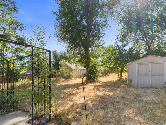 Expansive backyard featuring mature trees, a metal storage shed, and an additional smaller outbuilding