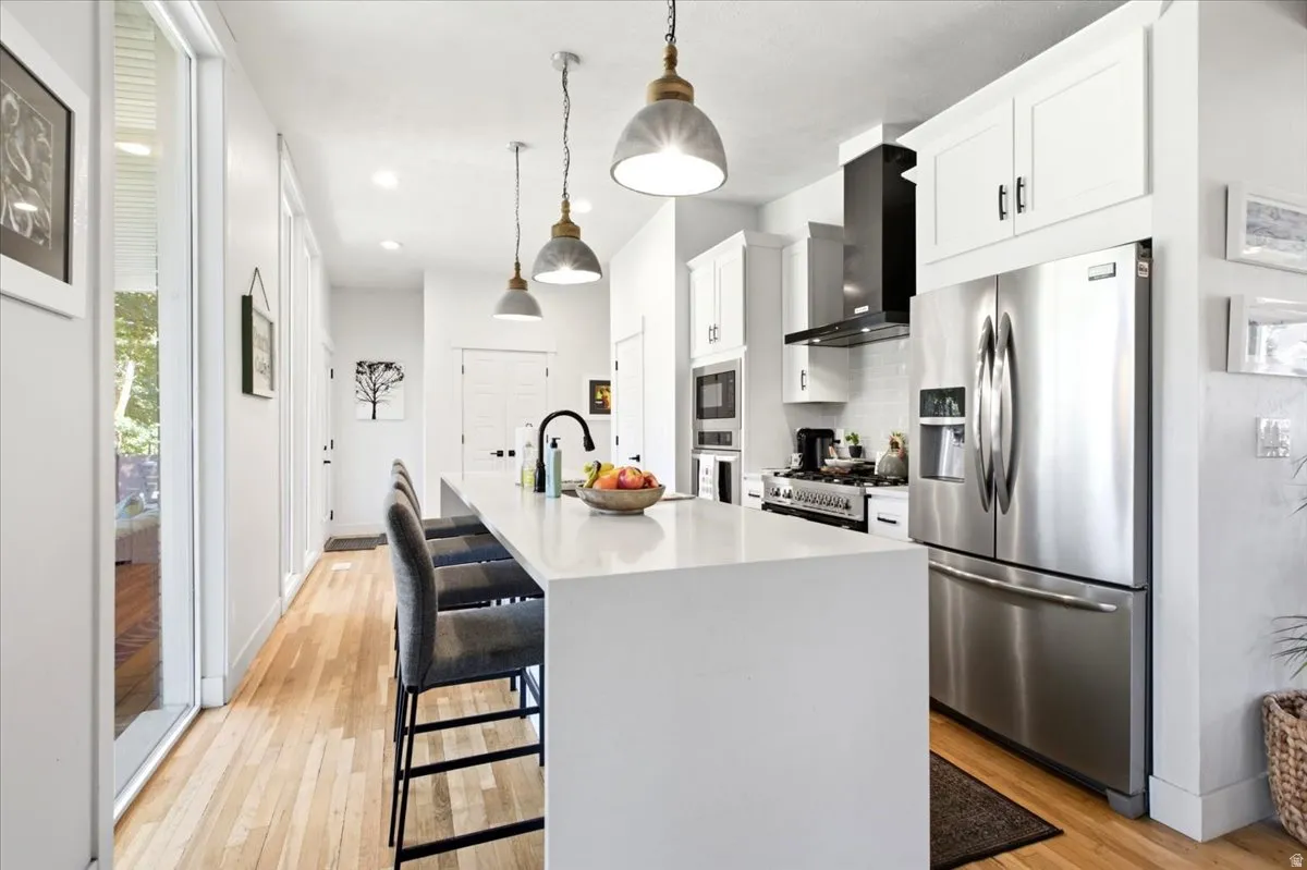 Contemporary kitchen featuring a large center island with seating, stainless steel appliances, white cabinetry, and wood-finish flooring