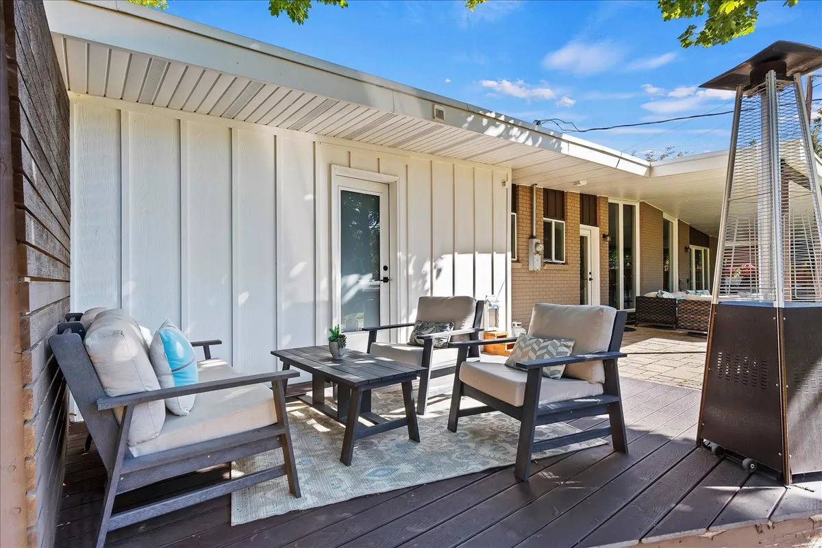 Expansive outdoor decking features a white board and batten wall, a covered patio area, and a glass-paneled exterior door