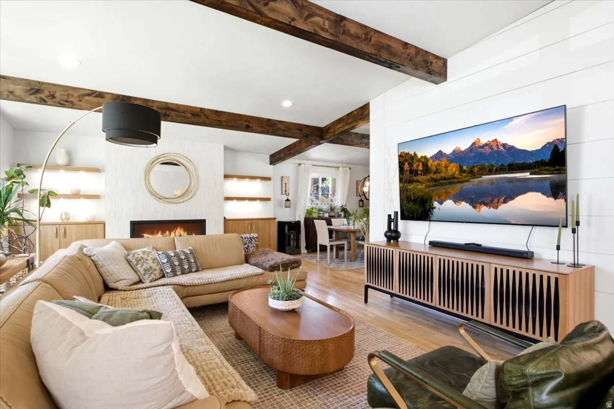 Living area featuring exposed wood ceiling beams, a built-in fireplace with textured surround, custom cabinetry, recessed lighting, and wood-finish flooring