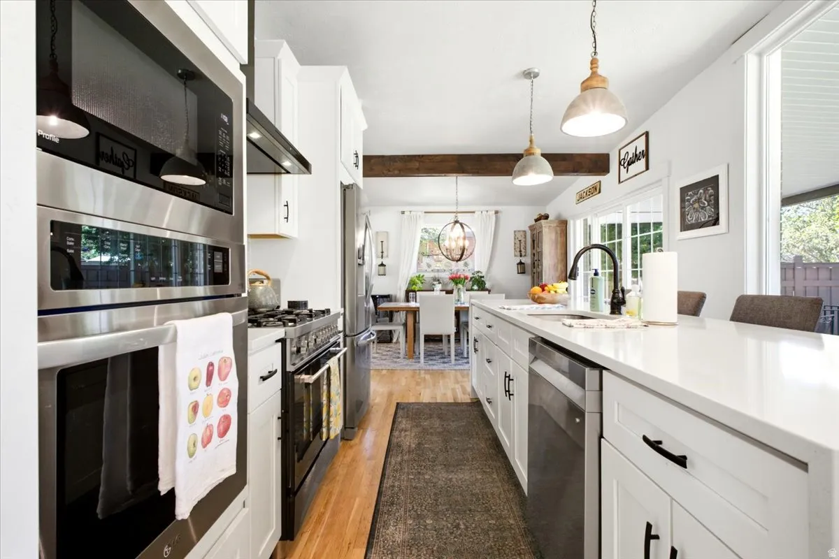 Modern kitchen featuring stainless steel appliances, white cabinetry, a large island with white countertops, wood-finish flooring, and recessed lighting