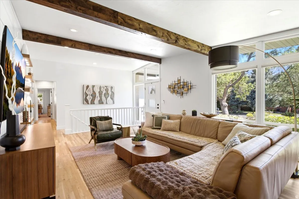 Bright living area featuring exposed wood beams, light wood-finish flooring, and expansive windows