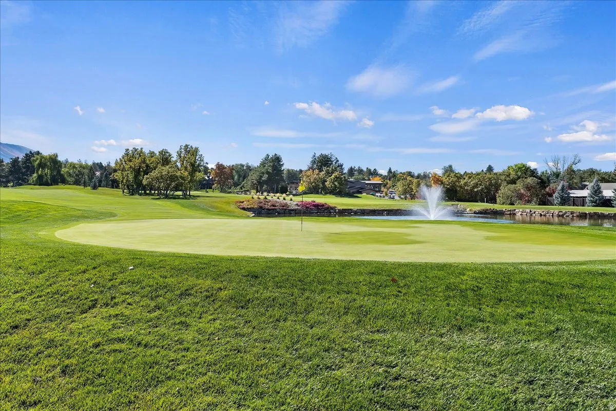 Expansive golf course green with manicured turf, a water feature with a fountain, and mature landscaping