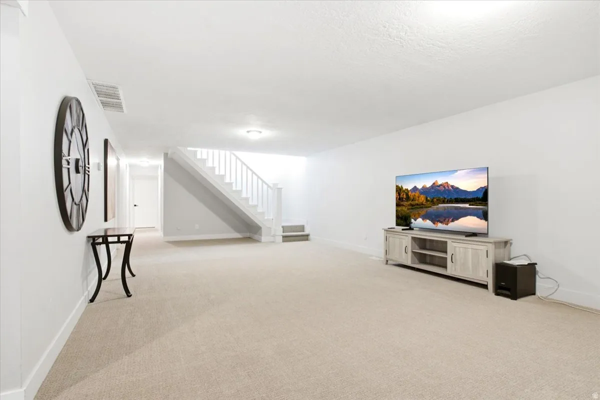 Spacious carpeted room featuring a white staircase with balusters, recessed lighting, and white baseboards