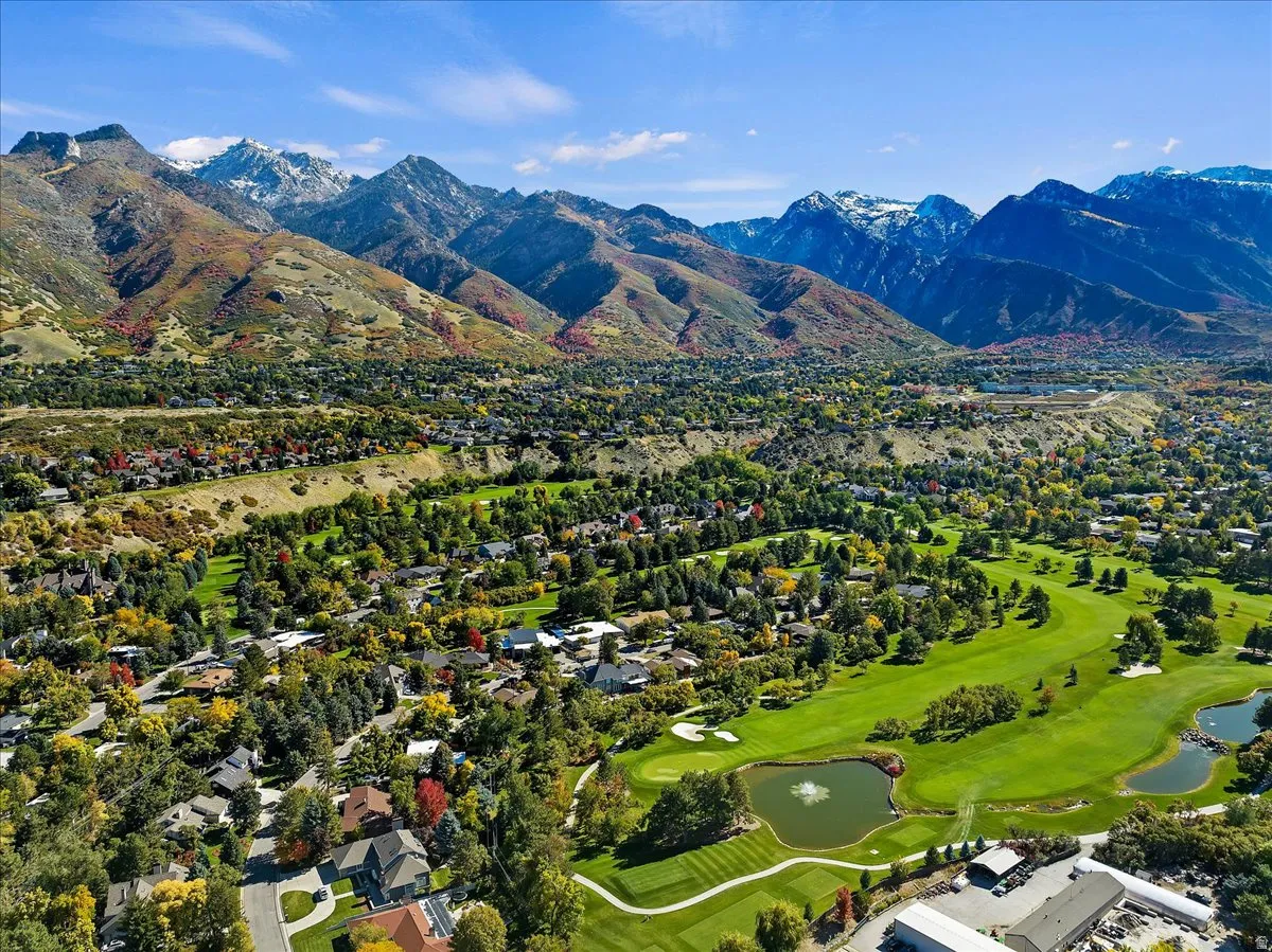 Expansive golf course with water features and lush landscaping, surrounded by residential areas and framed by majestic snow-capped mountains