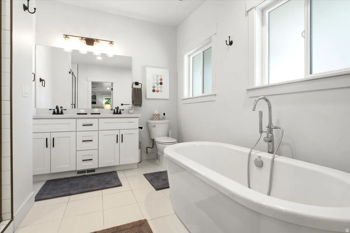 Bathroom featuring a freestanding soaking tub with a floor-mounted faucet, a double vanity with white cabinetry and dark hardware, a large wall mirror, and tiled flooring