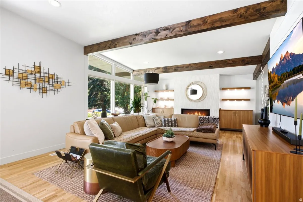 Living area featuring wood-finish flooring, exposed wood ceiling beams, and a fireplace with a textured surround