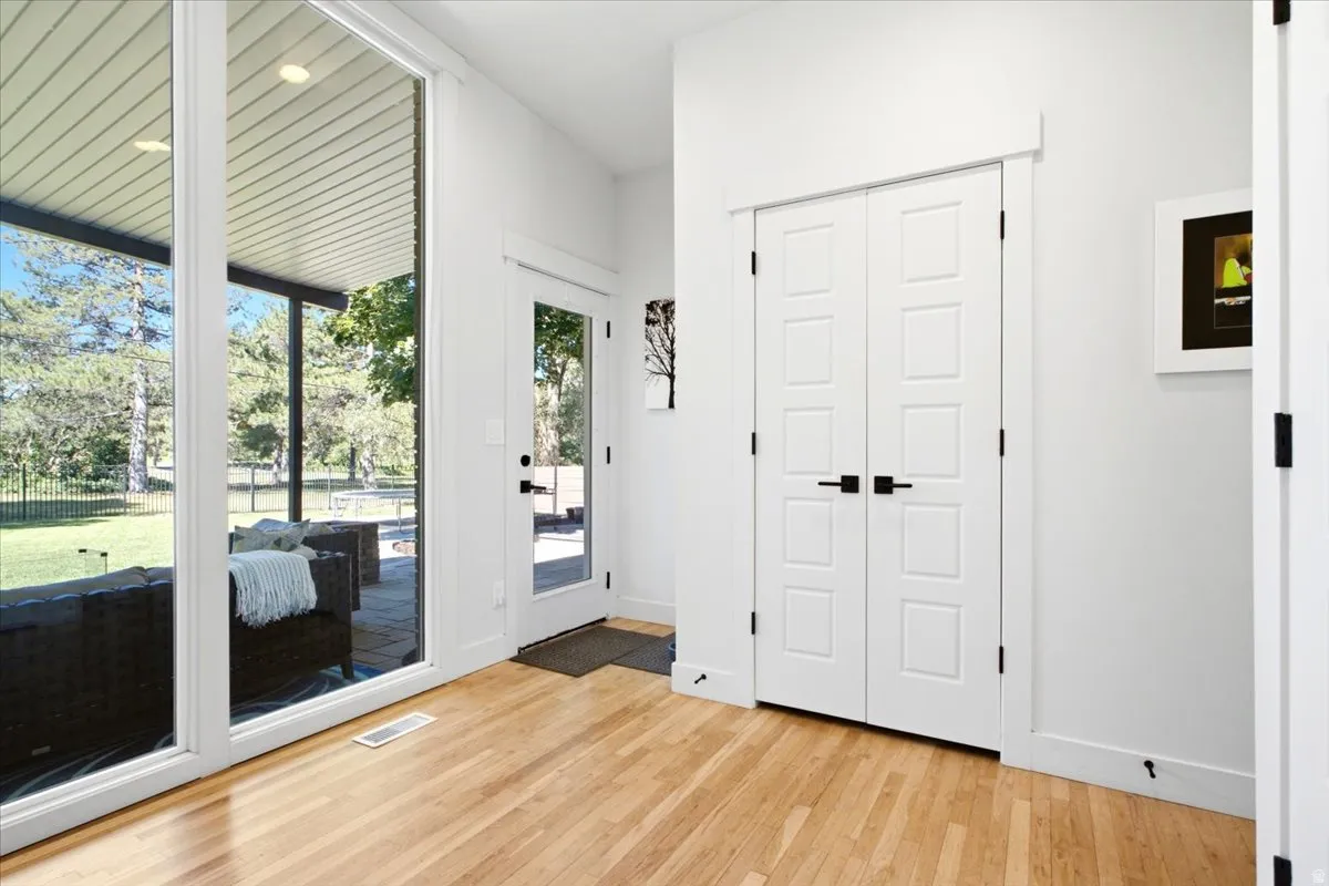 Hardwood flooring throughout entryway with white trim, white walls, and a modern white paneled double door