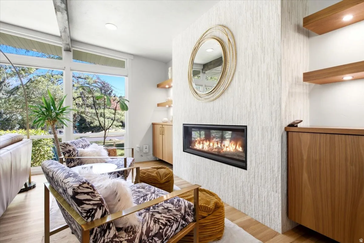 Living area featuring a textured fireplace wall with a linear fireplace insert, wood-finish flooring, built-in wooden cabinetry, floating wooden shelves with integrated lighting, and large windows