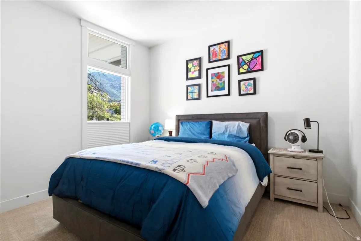 Bedroom featuring a large window with a transom, white window blinds, and light-colored carpet flooring