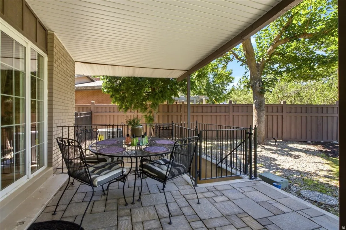 Covered patio featuring paver flooring, brick exterior, and a black wrought iron railing
