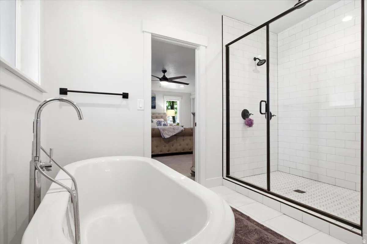 Freestanding soaking tub with a floor-mounted chrome faucet, alongside a glass-enclosed shower featuring subway tile surround, hexagon tile flooring, and matte black fixtures