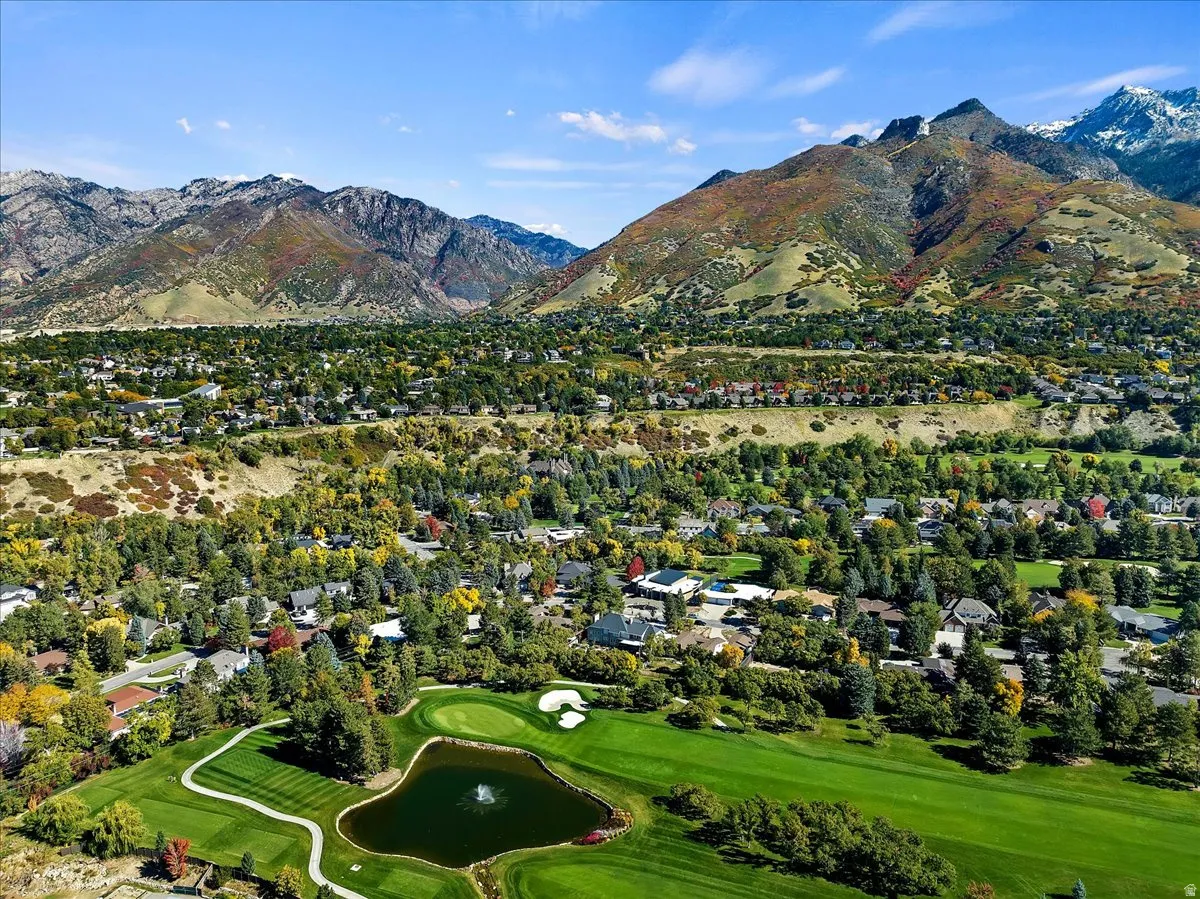 Aerial perspective showcasing a verdant golf course with a central pond and water feature, surrounded by mature trees and residential properties
